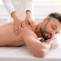 Female therapist rubbing joyful man shoulders at spa salon
